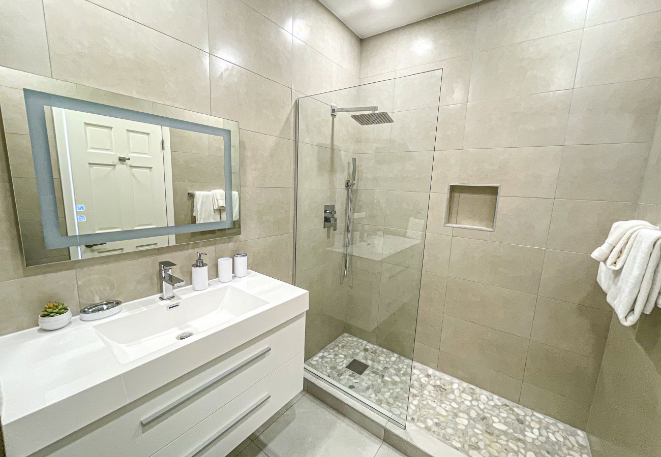 En-suite bathroom with a lighted and heated mirror, white vanity with drawers, and a large rainfall shower